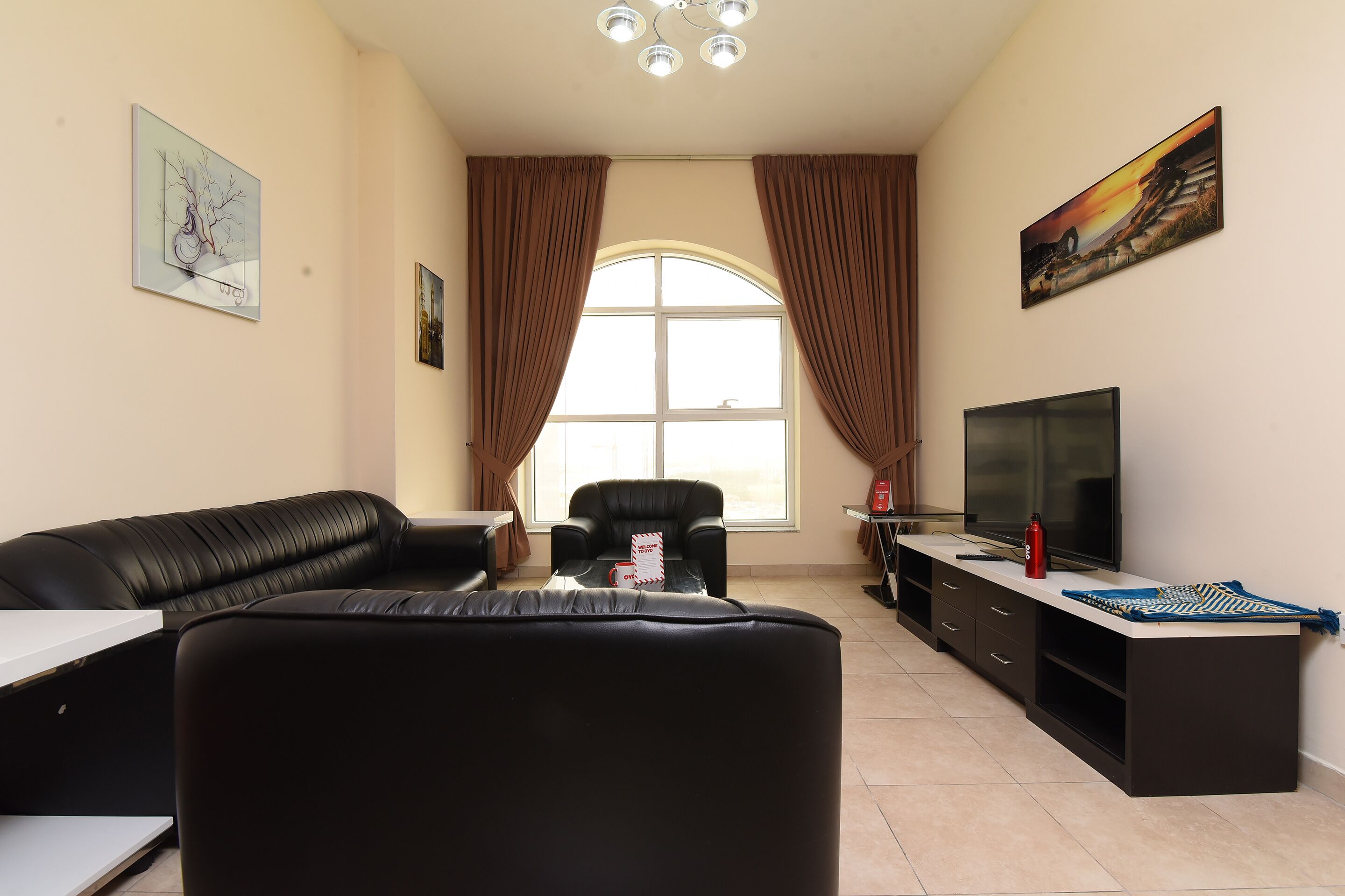 A living room with a black leather sofa, a TV, and a large window with curtains.