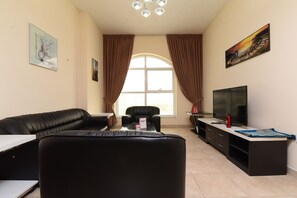 A living room with a black leather sofa, a TV, and a large window with curtains.