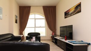 A living room with a black leather sofa, a glass coffee table, a TV, and a painting on the wall.