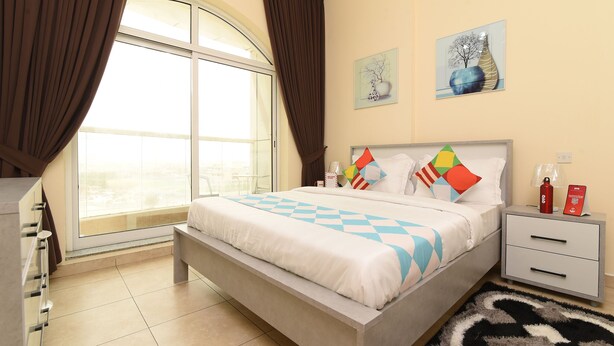 A modern bedroom with a large bed, a bedside table with a lamp, and a view of the city through a large window.