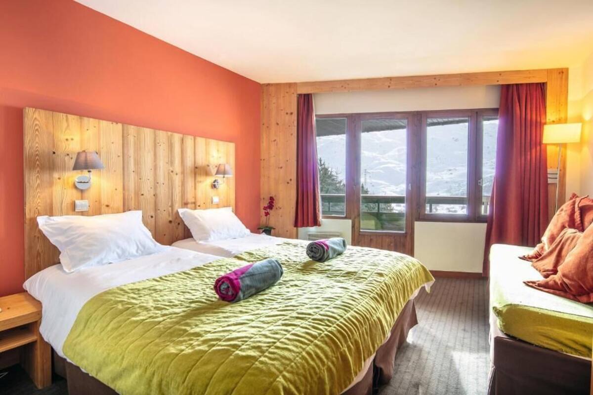 A hotel room with two beds, wooden headboard, large windows, and a view of mountains.