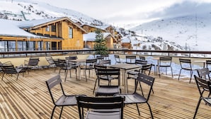 Terraza de madera con mobiliario exterior, con vistas a un paisaje montañoso nevado y un telesilla.