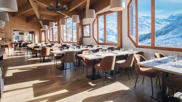 Un restaurante con interiores de madera, ventanas amplias y mesas dispuestas para comer.