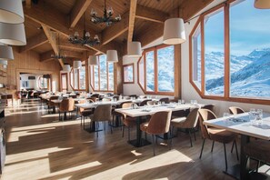 A restaurant with wooden interiors, large windows, and tables set for dining. - Hôtel Les Menuires Les Bruyères (Les Belleville)