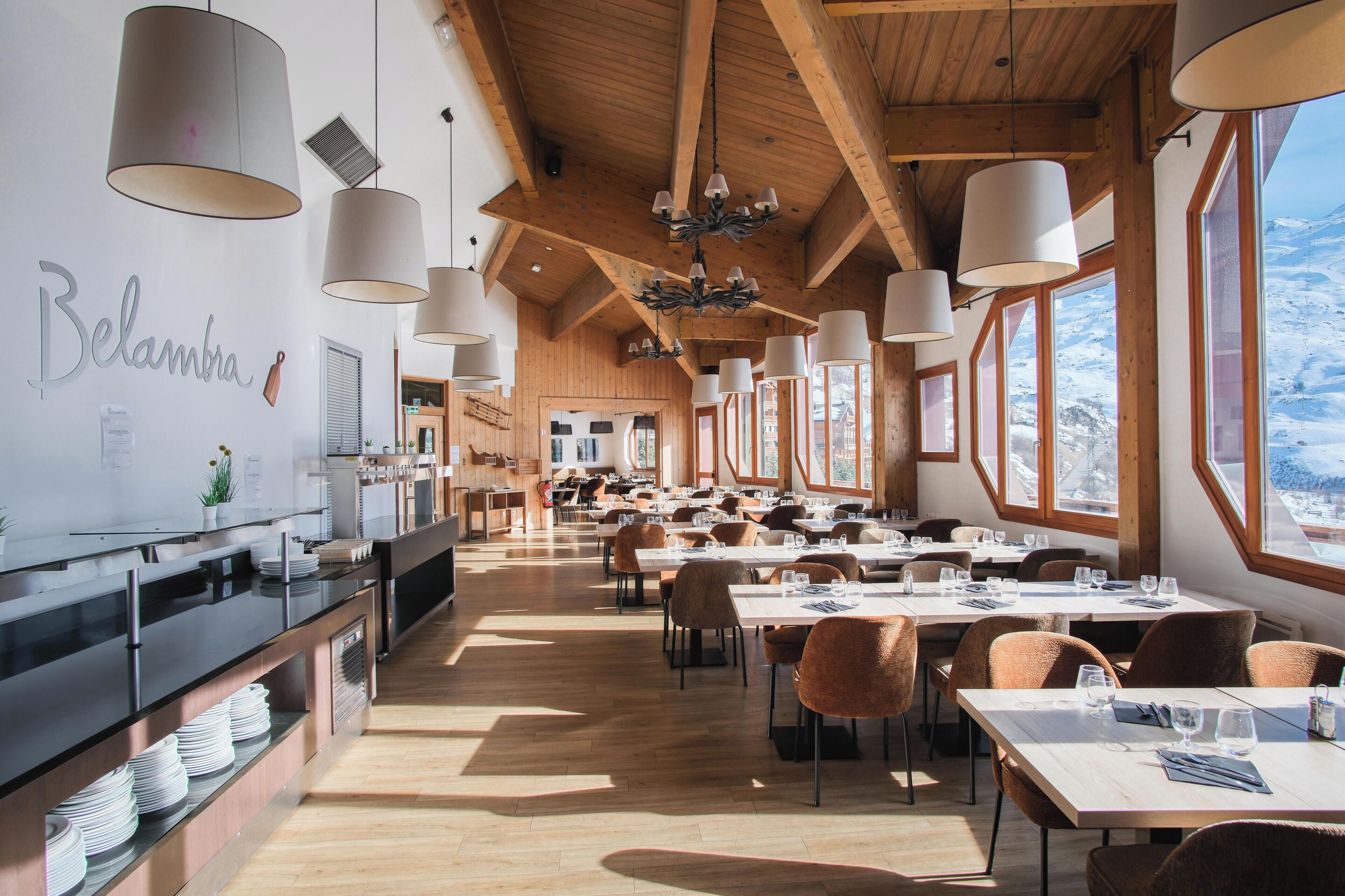 A spacious dining area with high ceilings, wooden beams, and large windows offering a view of the snowy landscape.
