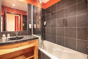 Un baño moderno con ducha envuelta en vidrio, bañera blanca y tocador de madera con lavabo.