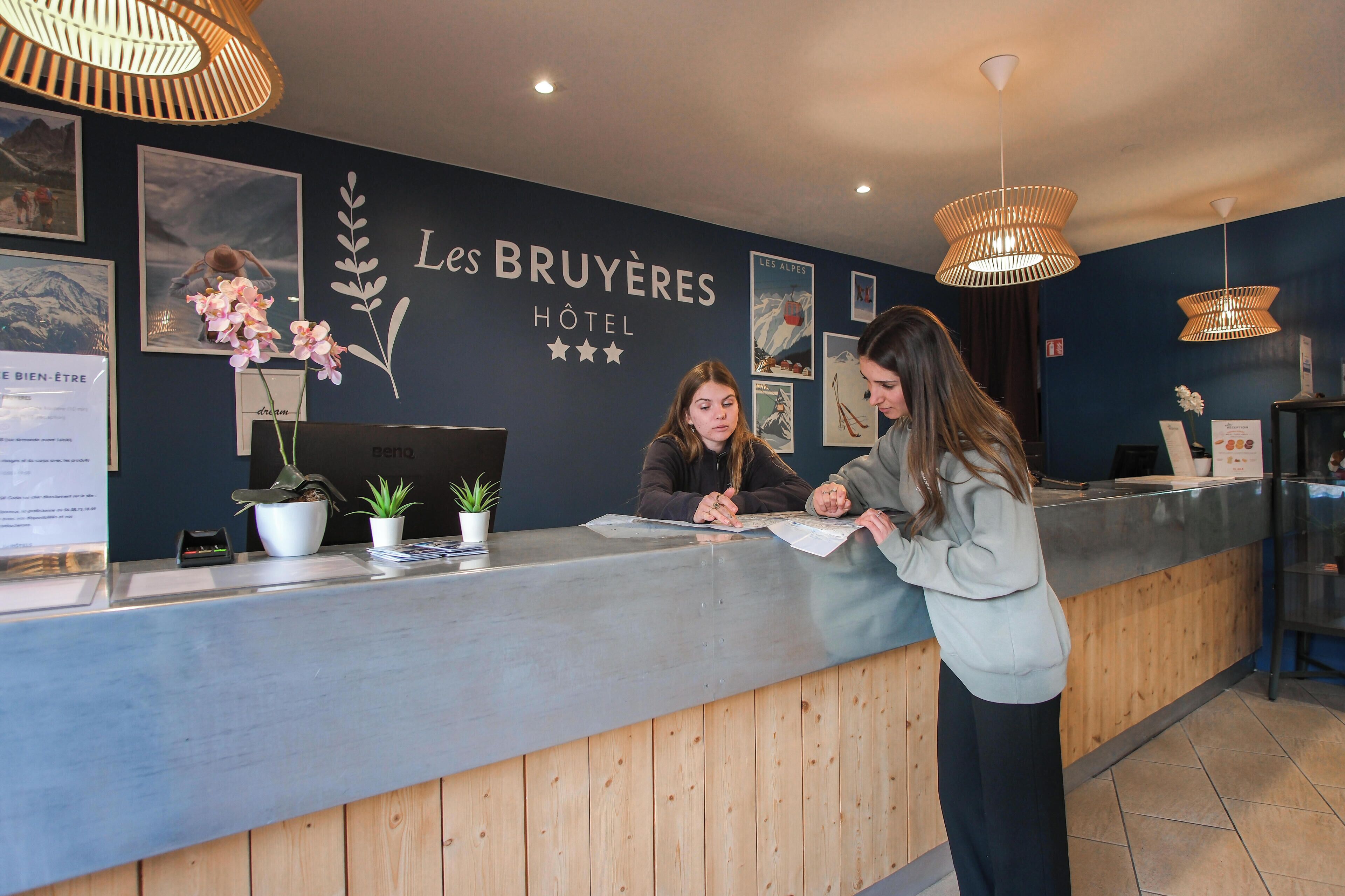Un mostrador de recepción de hotel con una pared azul oscuro, cuadros enmarcados y un letrero que dice 'Les Bruyères Hotel'.