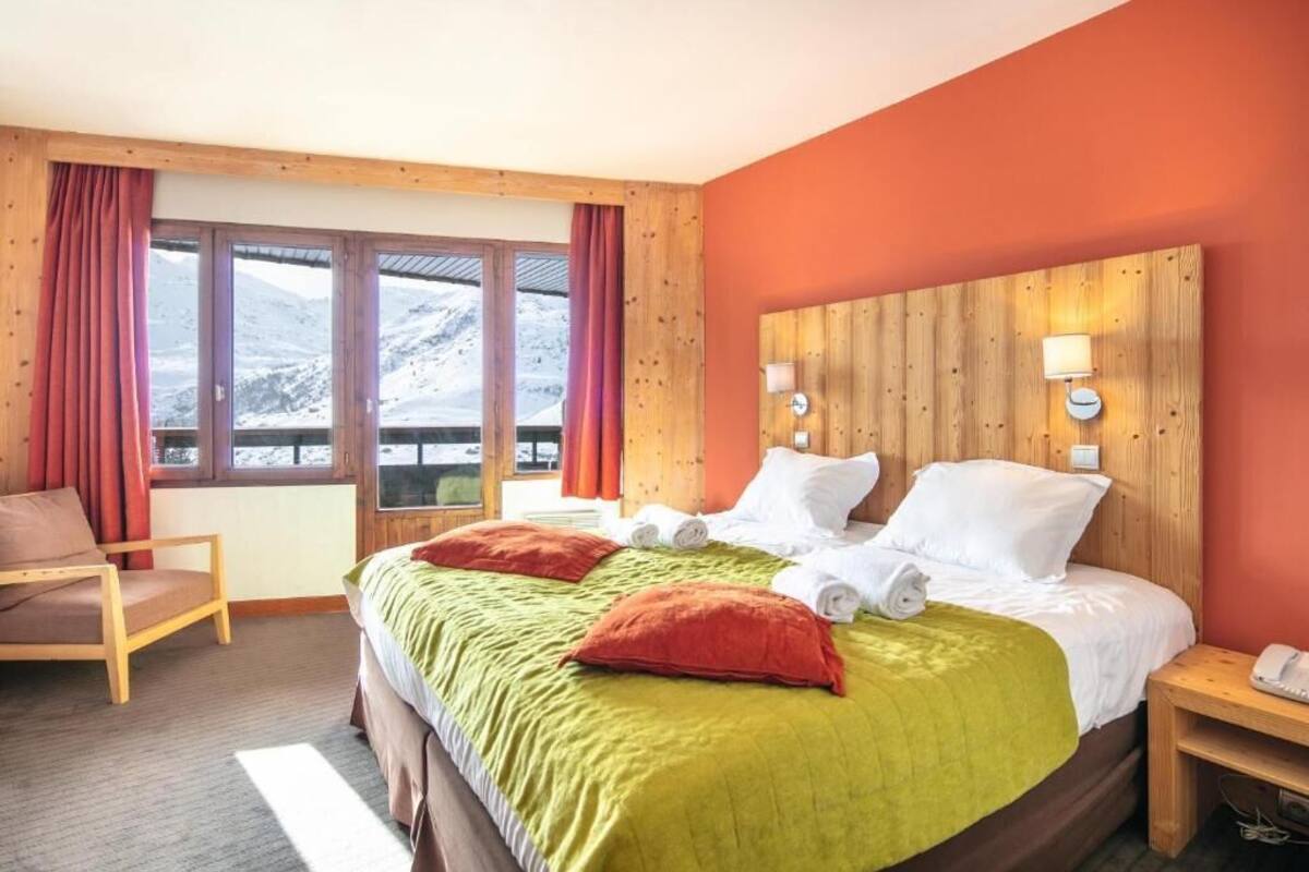 A hotel room with a bed, a chair, a nightstand, and a window with curtains.