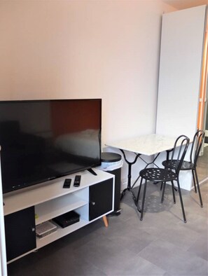 Una habitación moderna con televisión de pantalla plana sobre un mueble blanco, una mesita con dos sillas y una pizarra en la pared.