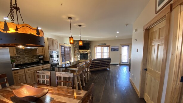 A spacious kitchen with wooden cabinets, a central island with stools, pendant lighting, and a stone fireplace.