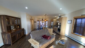 A spacious living room with a grey sofa, wooden coffee table, and a kitchen in the background.