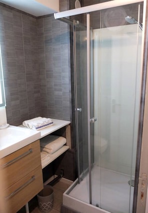 Een moderne badkamer met een glazen douchecabine, een wit aanrecht en een handdoekrek.