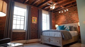 Un dormitorio con techo de madera, una cama con muchas almohadas, un escritorio y una ventana con cortinas.