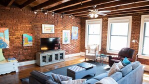 Una sala de estar con pared de ladrillo, televisor, sofá y sillón.