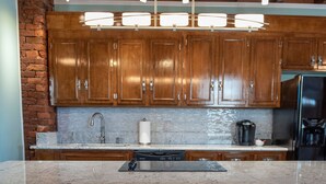 Una cocina con armarios de madera, encimera de mármol, un lavabo, una cafetera y cuatro taburetes blancos.