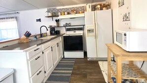 Een kleine keuken met witte kastjes, een zwarte oven, een witte koelkast en een magnetron op een houten tafel.