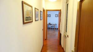 A hallway with wooden flooring, framed pictures on the walls, and a dining area in the background. - ..... SUPERCASONA PRATICA! (Sarzana)