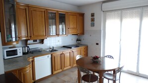 A kitchen with wooden cabinets, a microwave, a sink, and a dining area with a table and chairs.