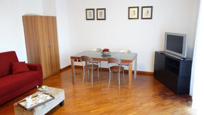 A living room with a red sofa, a dining table with chairs, a TV stand, and framed pictures on the wall. - ..... SUPERCASONA PRATICA! (Sarzana)