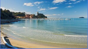 A coastal scene with a beach, calm sea, and buildings along the shore. - ..... SUPERCASONA PRATICA! (Sarzana)