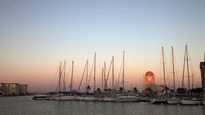 Een jachthaven met verschillende zeilboten afgemeerd, een opvallend gebouw met een koepel, en een heldere lucht.