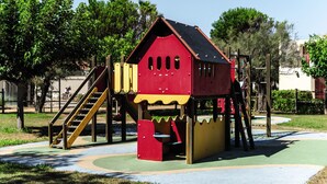 Een speeltuin met een rode en gele speelconstructie, inclusief een glijbaan en klimgedeelte.