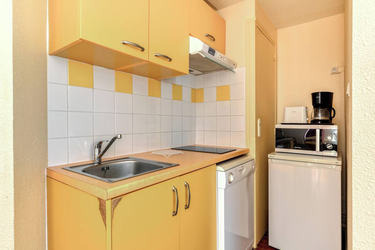 A compact kitchen with yellow cabinets, a white dishwasher, a microwave, and a coffee maker.