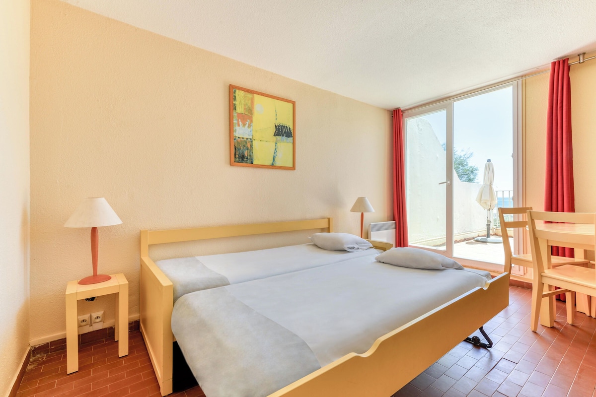 Un dormitorio con una cama, dos mesitas de noche, una silla, una mesa y una ventana con cortinas.