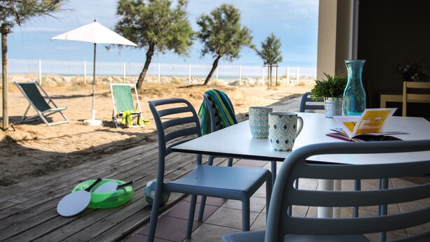 Een terras aan het strand met een tafel, stoelen en een strandparasol.