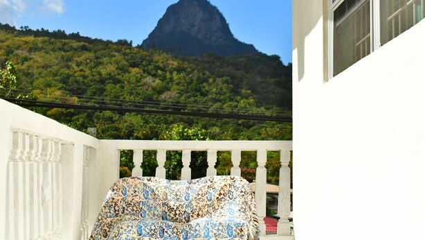 A balcony with a white balustrade, a floral-patterned sofa, and a view of a mountain.