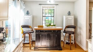 A kitchen with a central island, two bar stools, a window with a view, and a ceiling light fixture. - Cape Cod retreat , vacation memorable beaches , Good for families . (Barnstable)