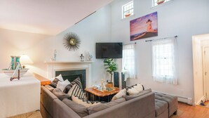 A living room with a fireplace, a sofa, a TV, and a painting of a lighthouse. - Cape Cod retreat , vacation memorable beaches , Good for families . (Barnstable)