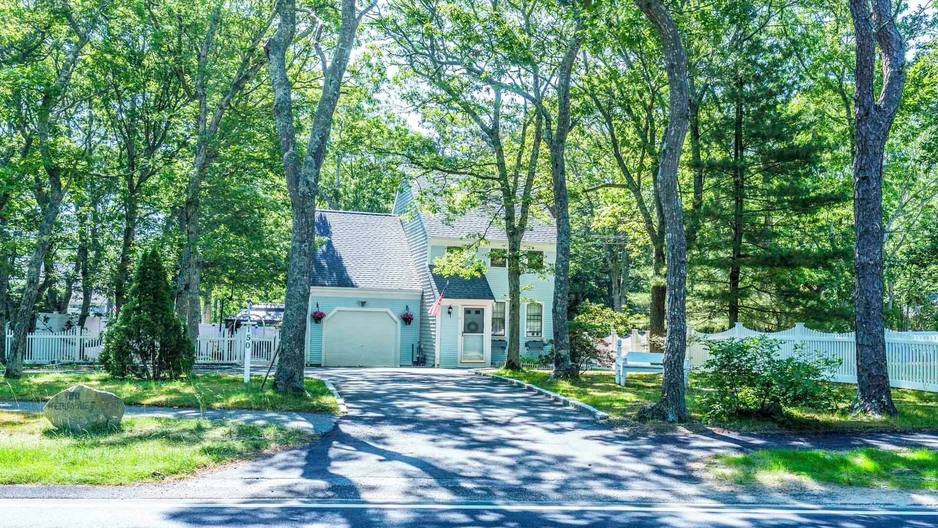 Ein Wohnhaus mit Auffahrt zu einer Garage, umgeben von hohen Bäumen und einem weißen Zaun.