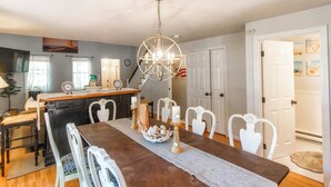 A dining area with a wooden table, white chairs, and a chandelier. - Cape Cod retreat , vacation memorable beaches , Good for families . (Barnstable)