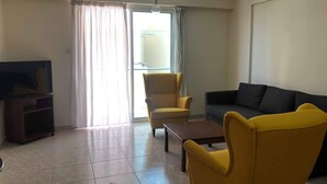 Een woonkamer met een flatscreen-tv, gele fauteuils, een donkere bank en een schuifdeur naar buiten.