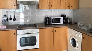 Een keuken met houten kastjes, een magnetron, een broodrooster, een koffiezetapparaat, een spoelbak en een wasmachine.