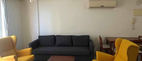 A living room with a dark grey sofa, two yellow armchairs, a wooden coffee table, and a dining table with chairs.