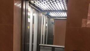 Een liftinterieur met metalen wanden, een glazen deur en een gestreept plafond.