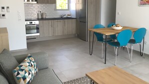 A modern kitchen with a built-in oven, a refrigerator, and a dining area with a wooden table and blue chairs. - Calvi bright T3 top floor 65m2 panoramic view, 4 people, 2 bedrooms, parking (Calvi)