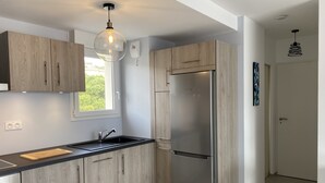 A modern kitchen with wooden cabinets, a stainless steel refrigerator, a black countertop, and a pendant light. - Calvi bright T3 top floor 65m2 panoramic view, 4 people, 2 bedrooms, parking (Calvi)