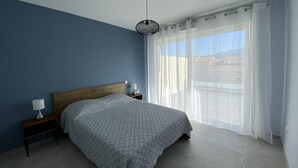 A bedroom with a bed, bedside tables, a hanging light fixture, and a large window with sheer curtains. - Calvi bright T3 top floor 65m2 panoramic view, 4 people, 2 bedrooms, parking (Calvi)