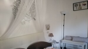 A bedroom with a bed, a bedside table, a lamp, a bench, and a wall decoration.