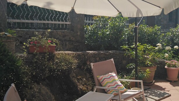 An outdoor patio with two lounge chairs, a large umbrella, and potted plants.