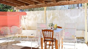 Une terrasse extérieure avec un sol en pierre, des meubles en bois et un espace couvert doté d’un plafond en bois.