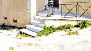 Un immeuble de deux étages avec une façade beige, des volets blancs et un petit balcon doté d’une rambarde en métal.