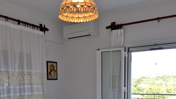 Une chambre à coucher avec un lit, une table de chevet, une lampe rouge, un tableau au mur et une vue sur le balcon extérieur.