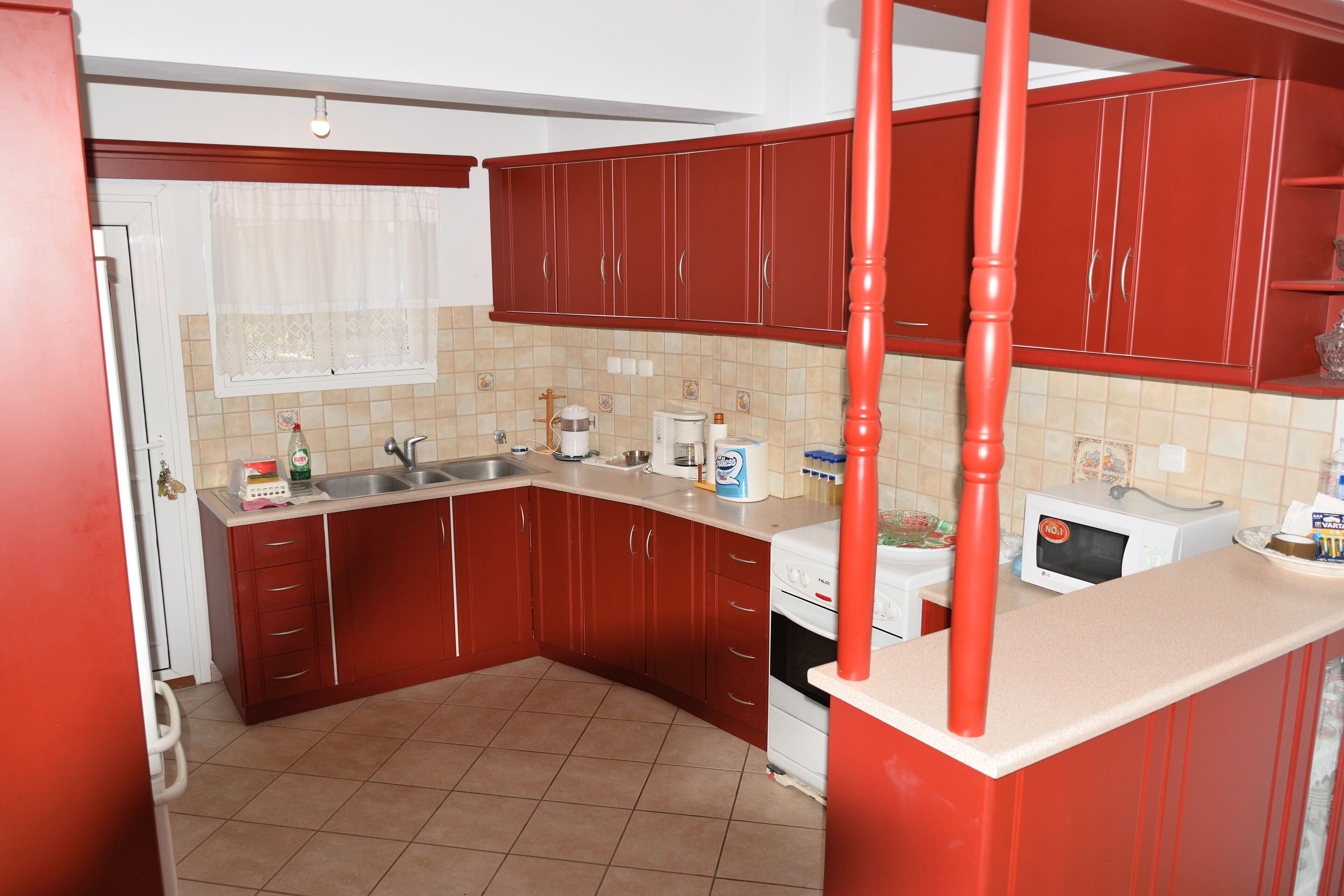 Una cocina con armarios rojos, un refrigerador blanco, un microondas y un lavamanos.