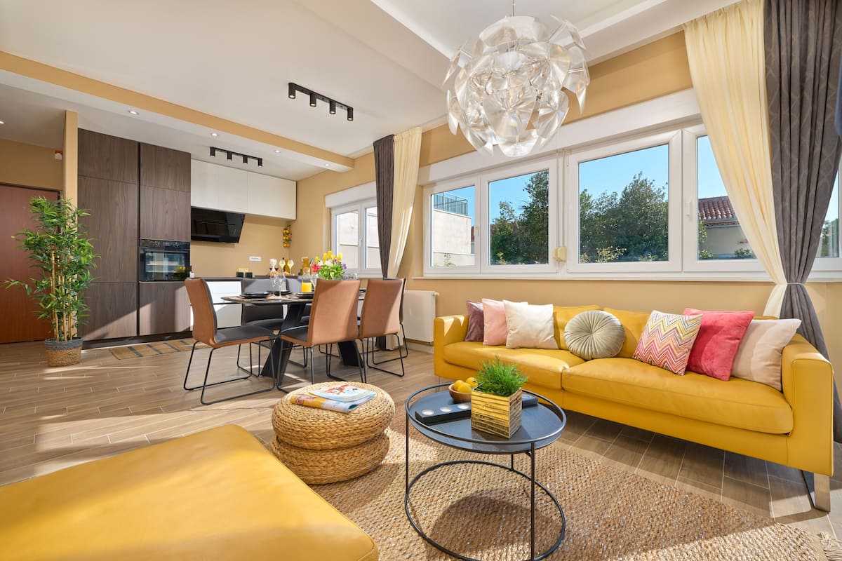 A modern living room with a yellow sofa, dining area, and kitchen.