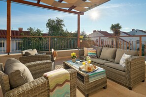 A covered outdoor seating area with wicker furniture, a table with breakfast items, and a view of the neighborhood.