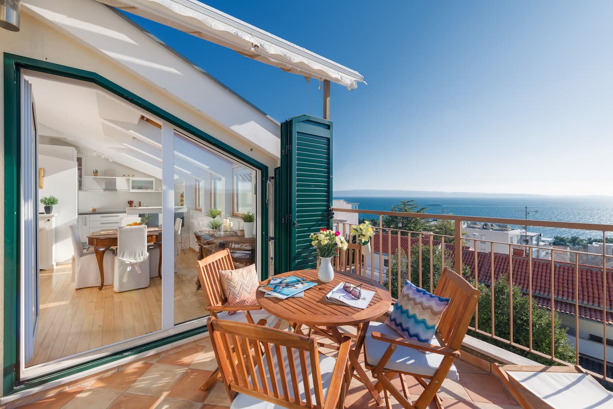 A wooden table and chairs on a balcony with a view of the sea.